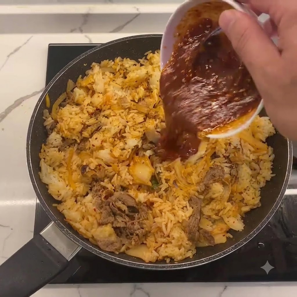 Special sauce being poured from a small white bowl into the center of the pan containing fried rice, kimchi, and beef.