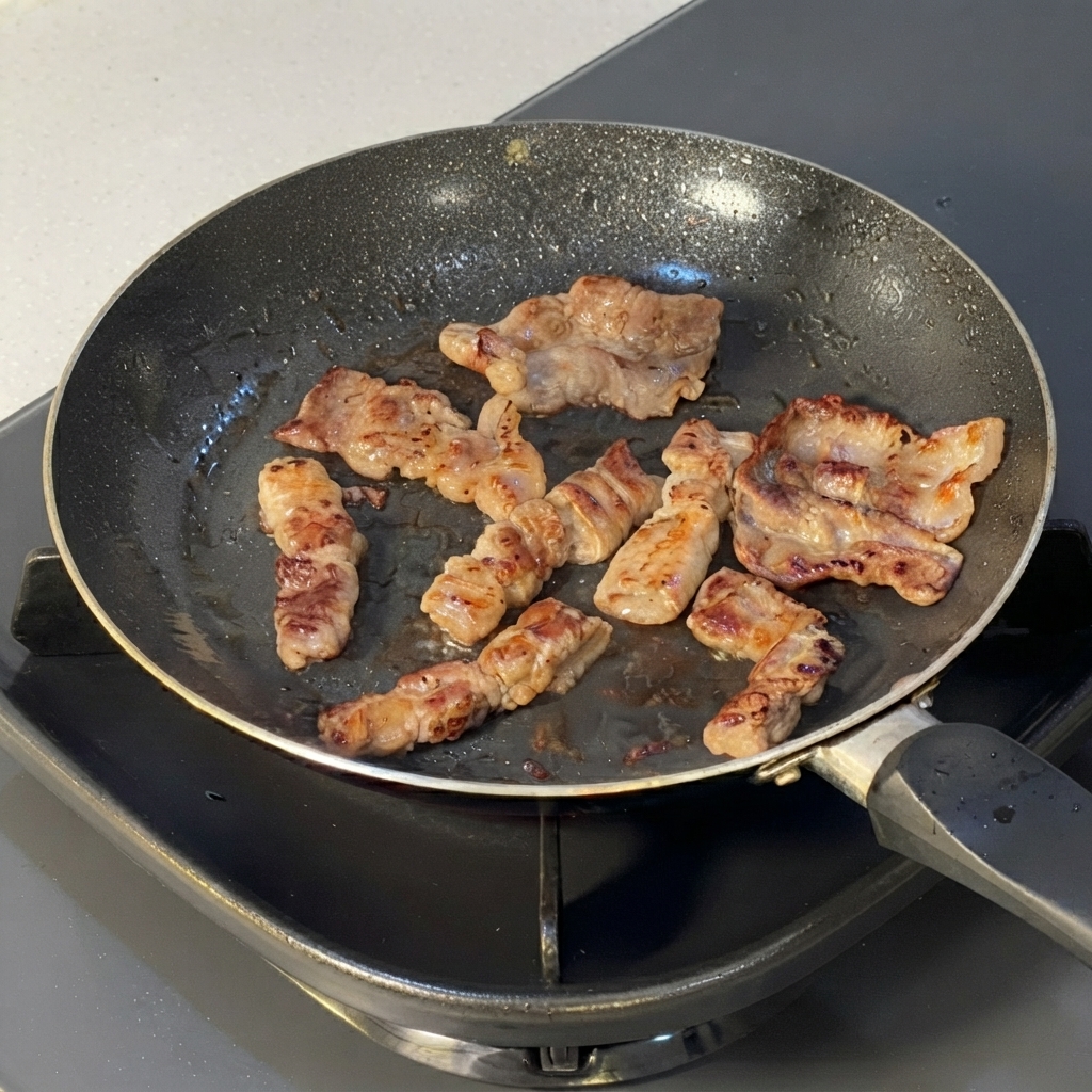 Cooked beef slices being cut into smaller segments with kitchen scissors inside a frying pan.