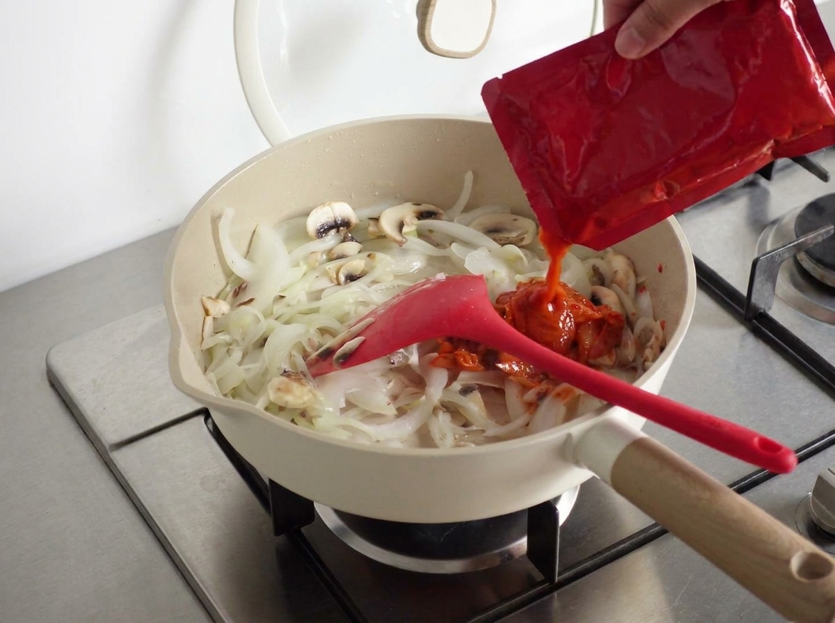 A spoonful of Korean spicy paste being added to the mixture in the pan.