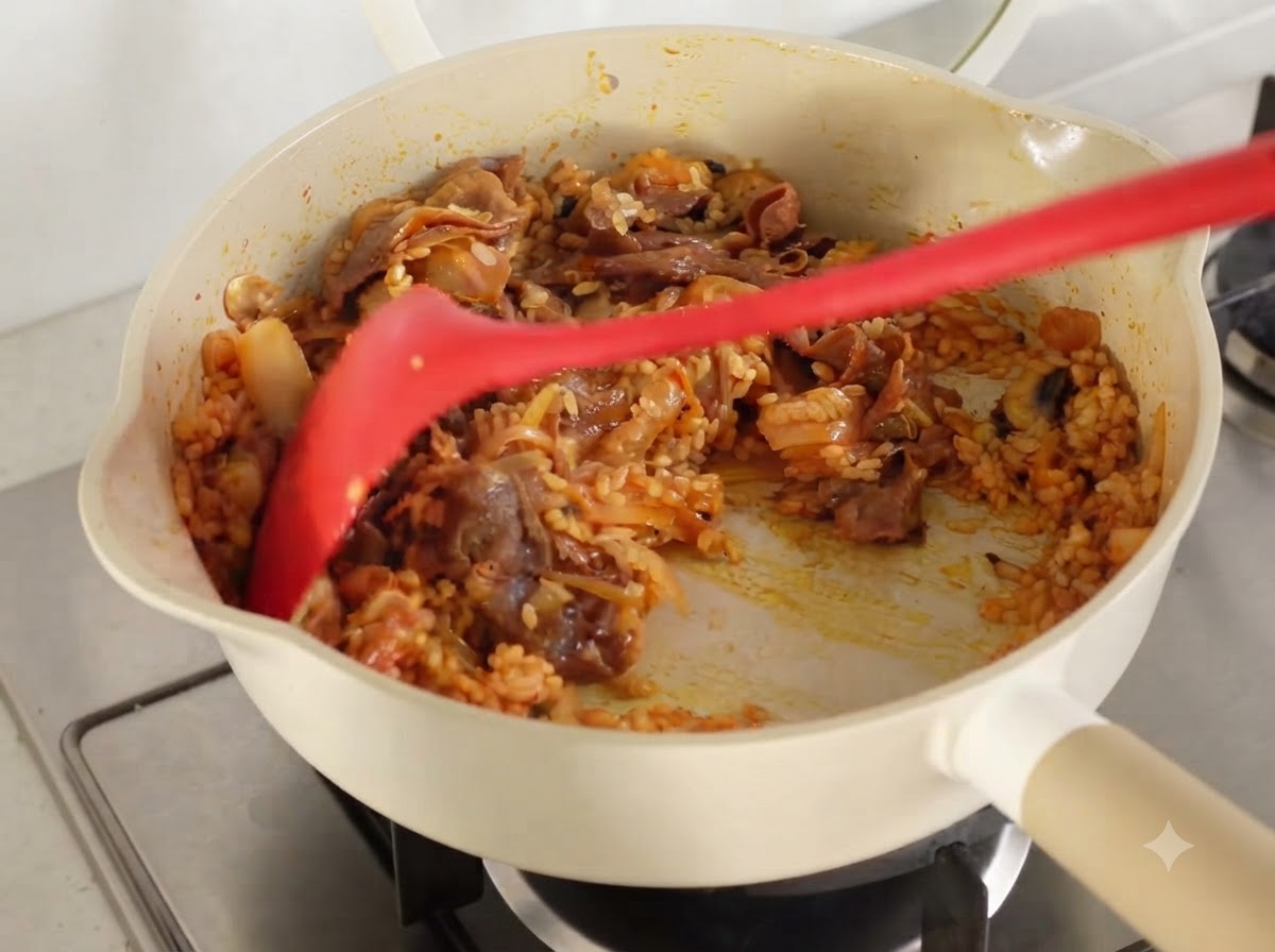 All the ingredients and rice being thoroughly stir-fried together until coated with kimchi juice in a pan.