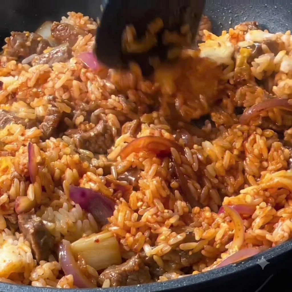 Rice, beef, and vegetables being mixed together thoroughly with a spatula in the pan.