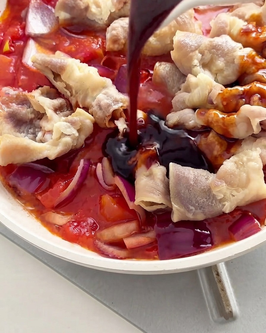 Dark sauce being poured from a spoon onto the beef rolls and tomatoes inside a white pan.