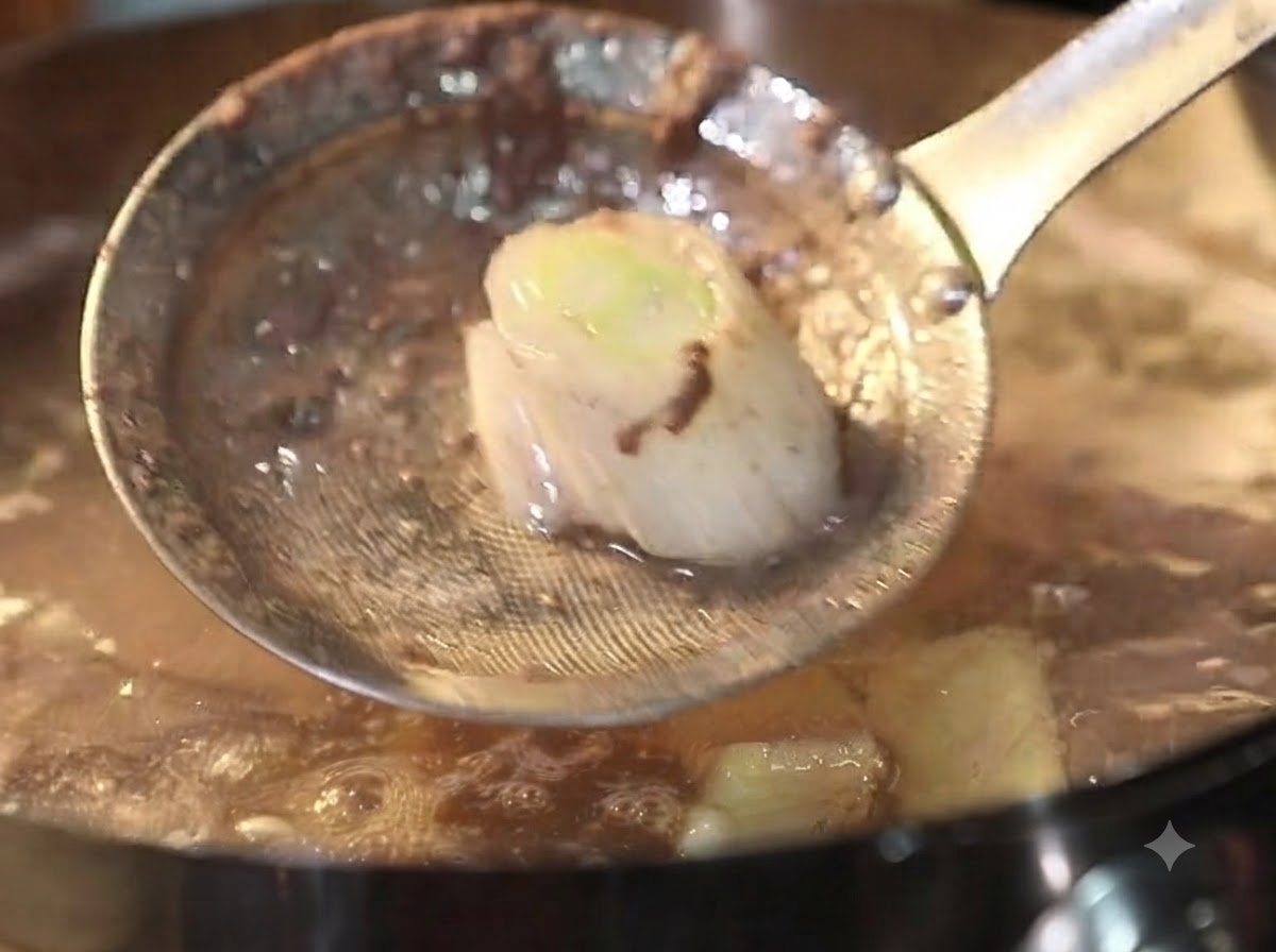 A metal skimmer scooping foam and debris out of a bubbling pot of beef broth.