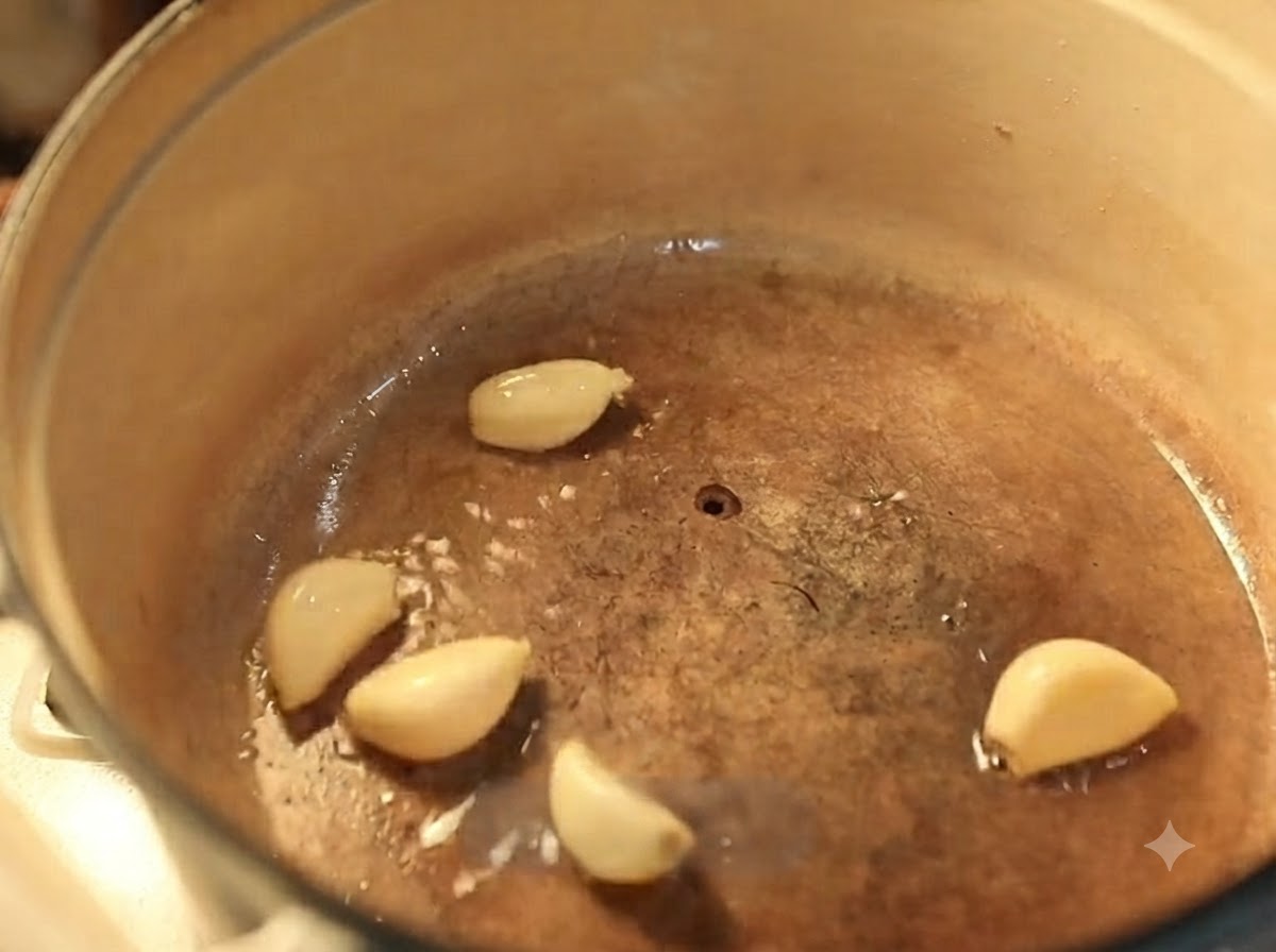 Garlic cloves frying in hot oil inside an enameled cast iron pot.