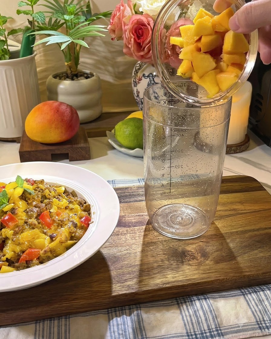 Fresh peach chunks, honey, and lemon slices being poured into a tall transparent mixing glass.