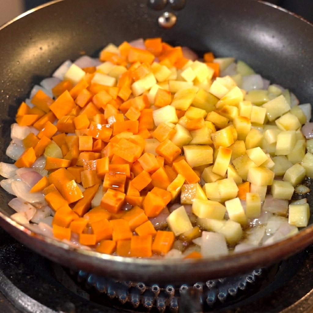 Dark soy sauce being poured onto diced carrots and potatoes in a skillet.