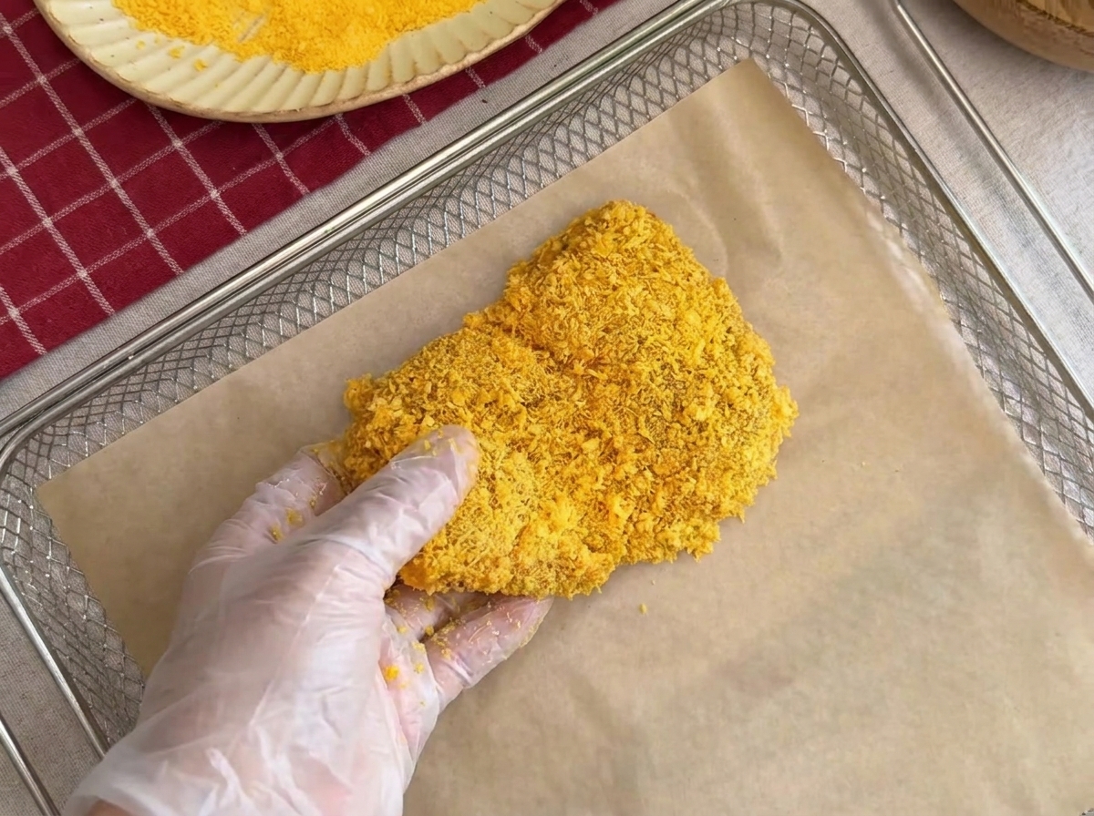 A breaded pork chop being placed carefully onto a parchment paper lined wire rack.