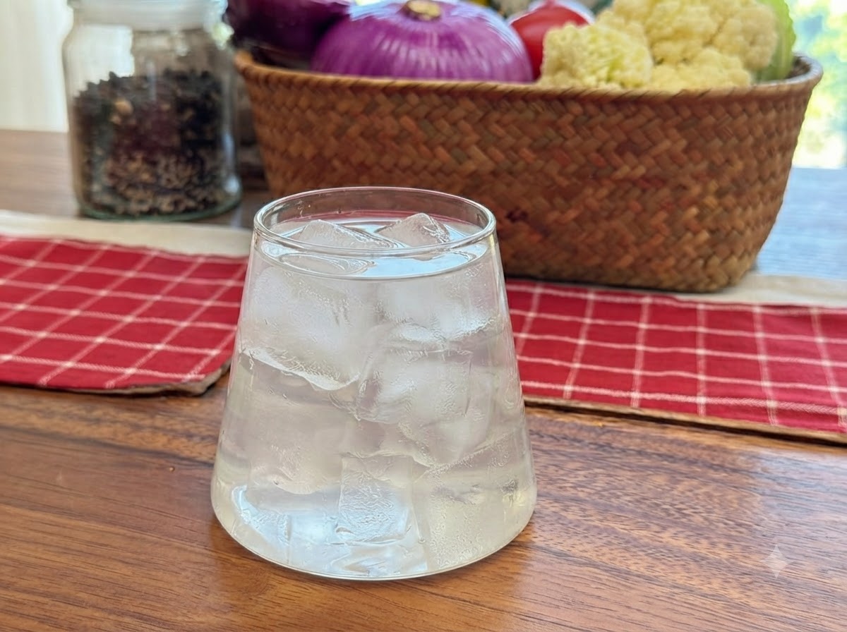 Coconut water being poured into a clear glass filled with ice cubes.