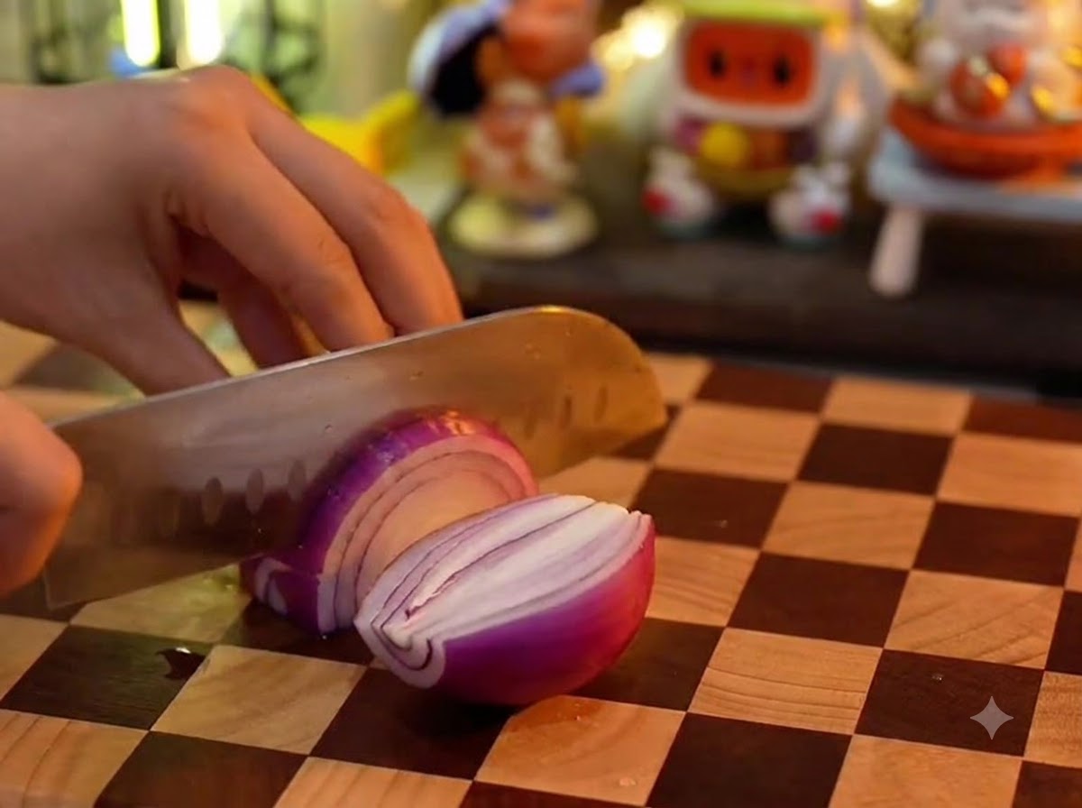 A kitchen knife slicing a red onion on a wooden checkered cutting board.