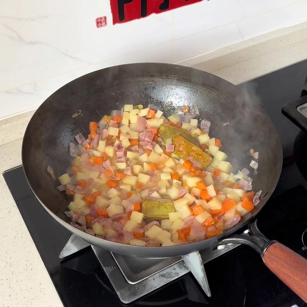 Diced potatoes and carrots being mixed with onions inside a wok.