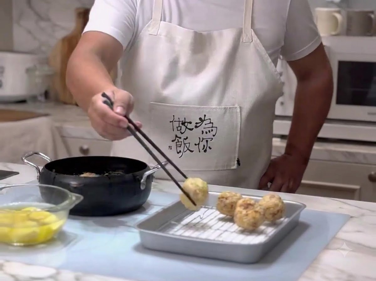 Meatballs being removed from hot oil using chopsticks and placed onto a wire draining rack.