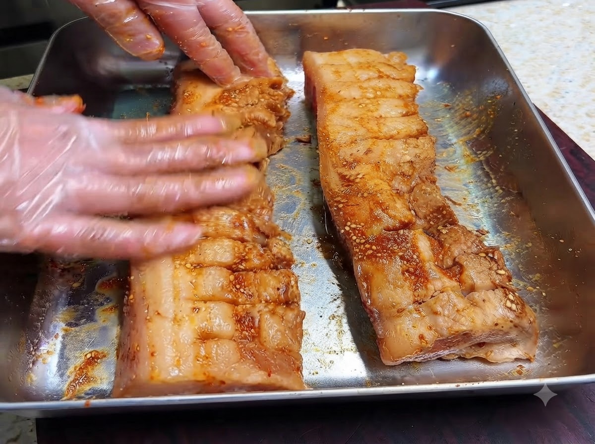 Gloved hands massaging dark marinade and dry spices into the scored surface of two pork belly strips.