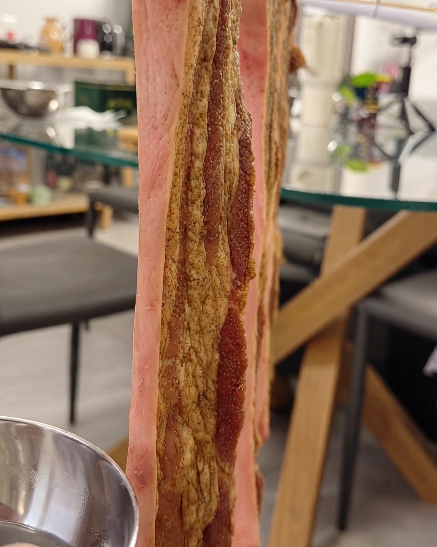 Pork belly hanging vertically on a rack while being brushed with crispy skin water on the skin.