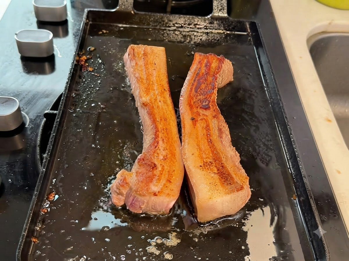 Thick pork belly strips being cut into smaller pieces with kitchen shears on the grill pan.