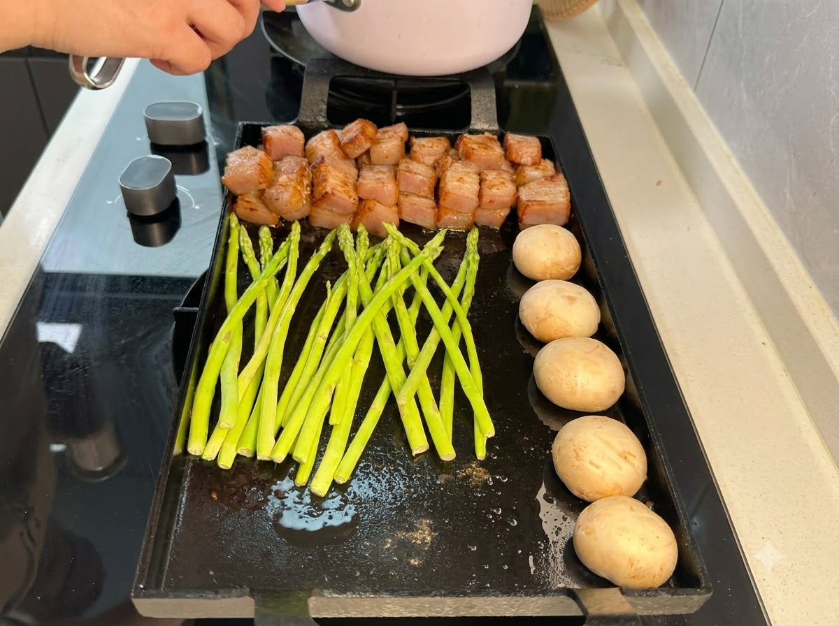 Fresh green asparagus spears laid out on the grill pan next to pork and mushrooms.