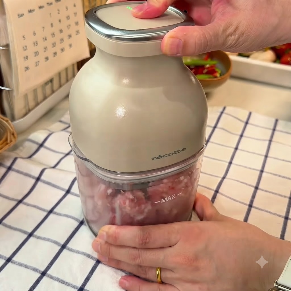 Pork pieces being chopped into textured minced meat using a small electric food chopper.