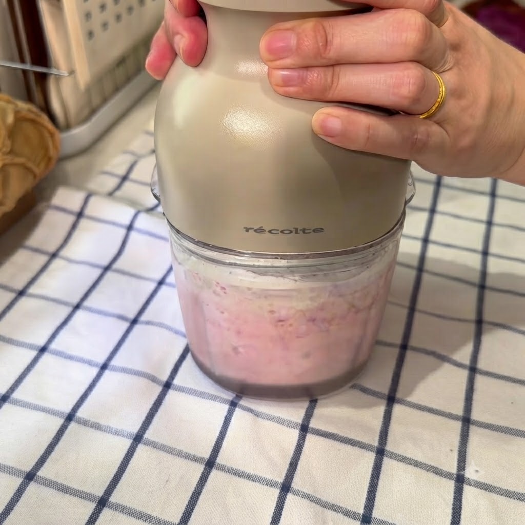 A food processor blending a pink mixture of frozen watermelon, ice water, and condensed milk.