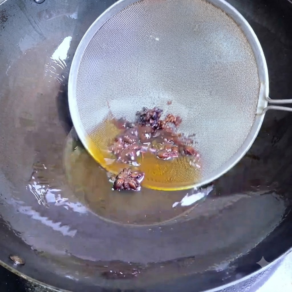 A wire strainer scooping dark star anise and Sichuan peppercorns out of hot oil in a wok.