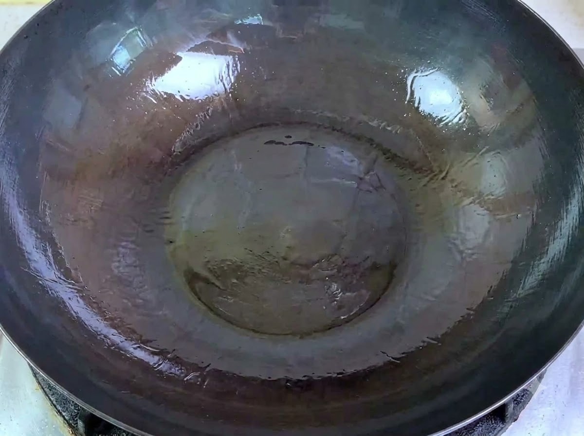 Raw minced pork being poured from a bowl into a large wok with hot oil.