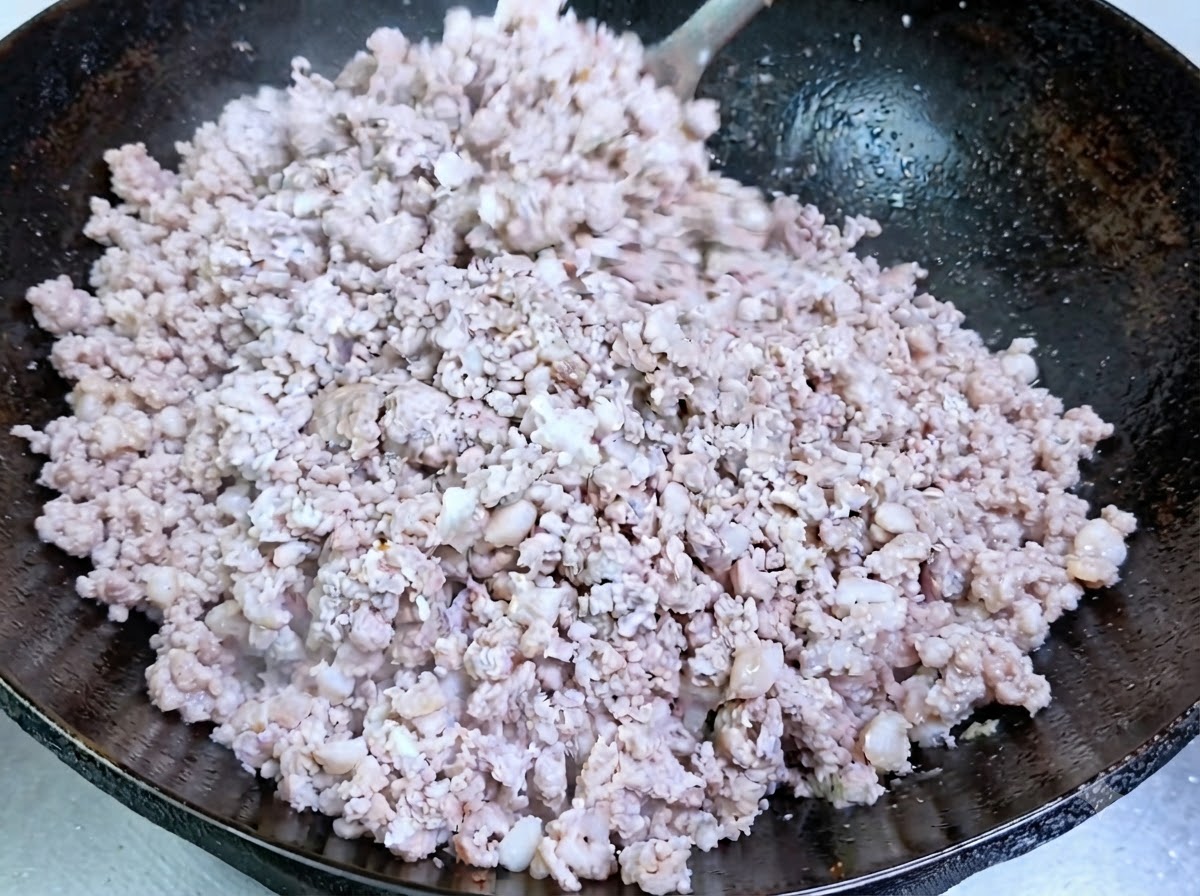 Minced pork cooking and turning opaque in a seasoned wok.