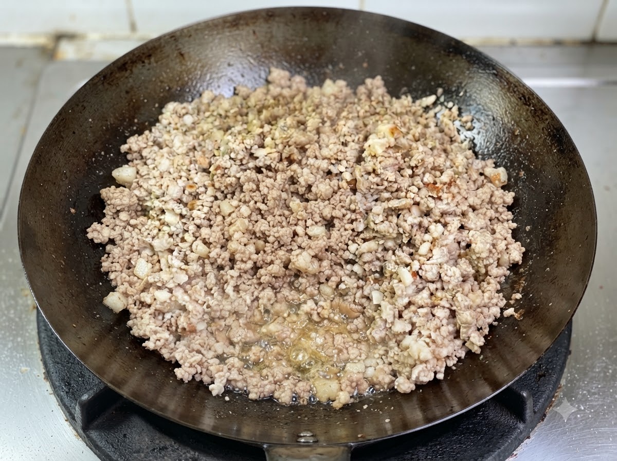 Minced pork browning in a wok with visible rendered oil bubbling at the base.