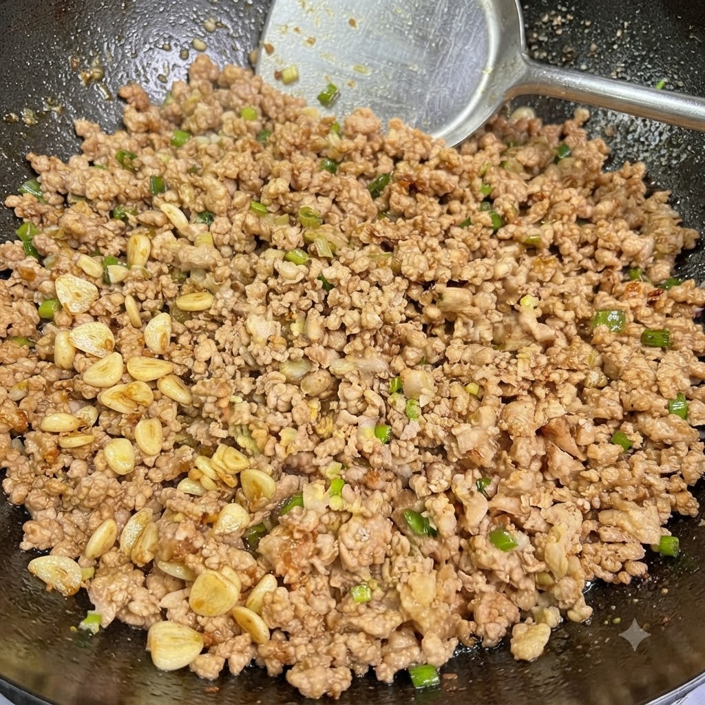Cooked minced pork mixed with scallions and garlic being stirred in a wok with a spatula.