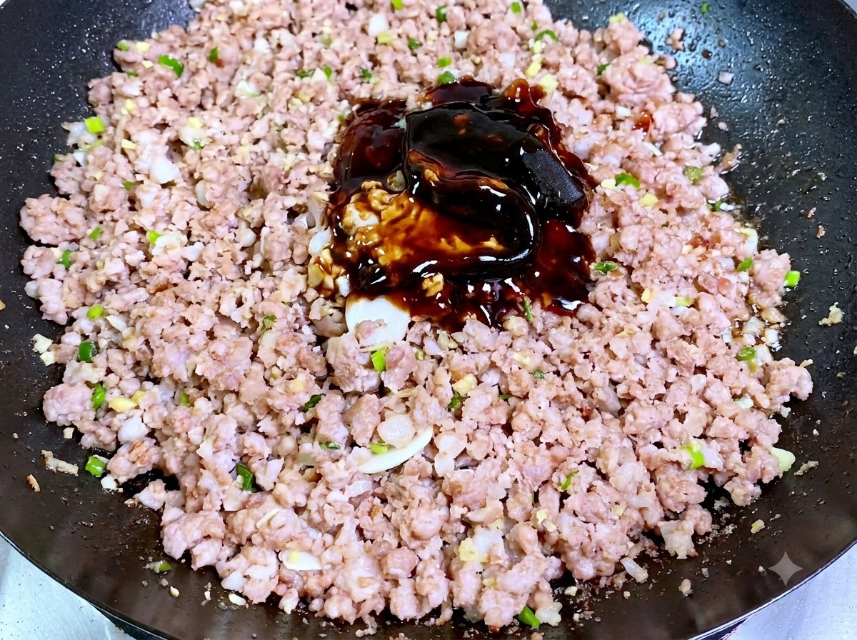 A heap of dark soybean pastes and sauces piled directly on top of cooked minced pork in a wok.