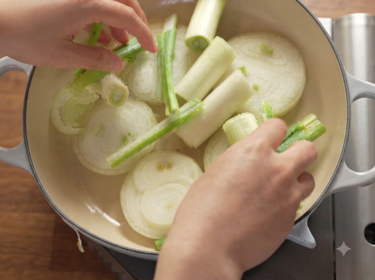 Slices of onions, green onions, and apples neatly arranged inside a heavy Dutch oven.