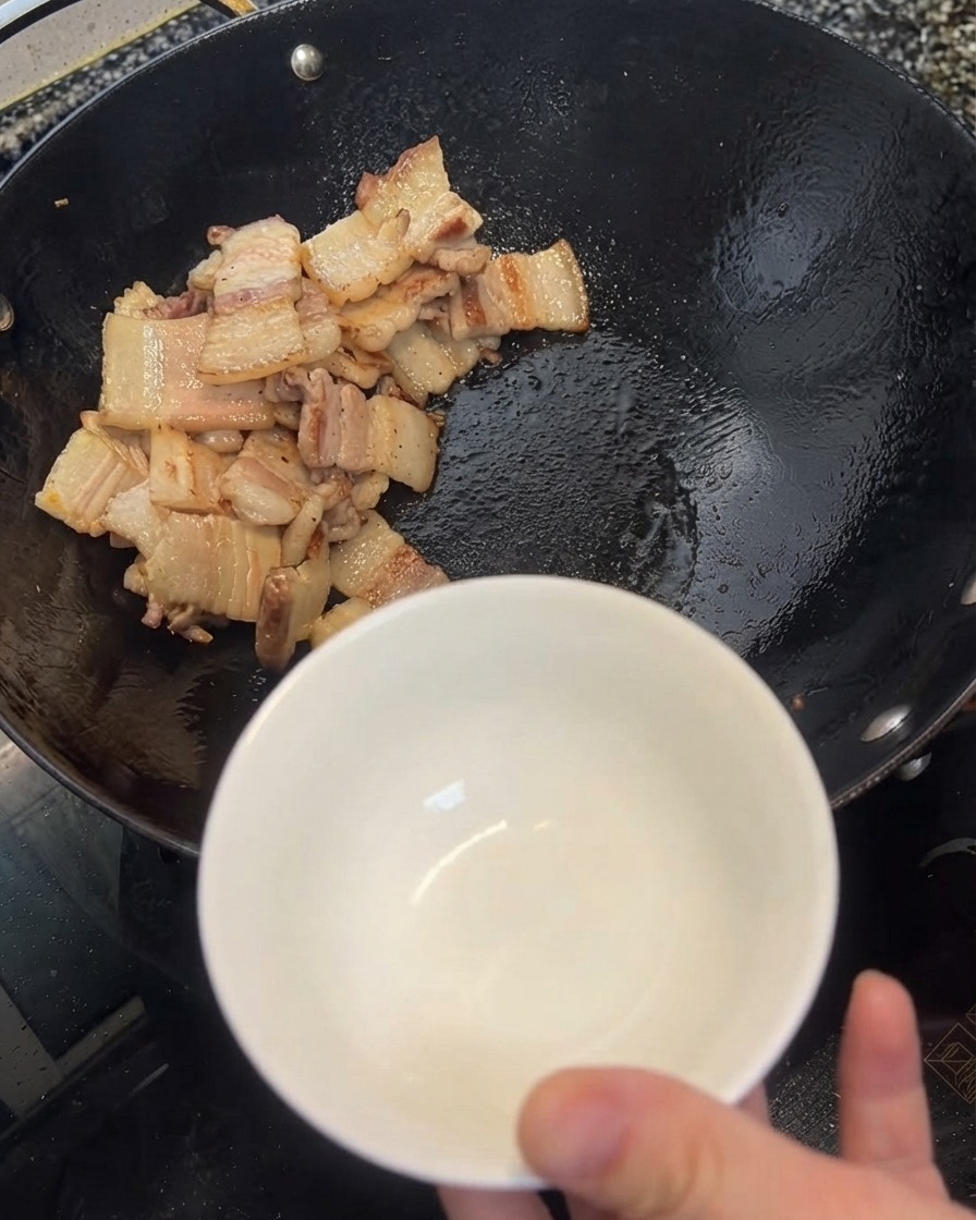 Excess oil being scooped from the wok into a white bowl using a spatula.