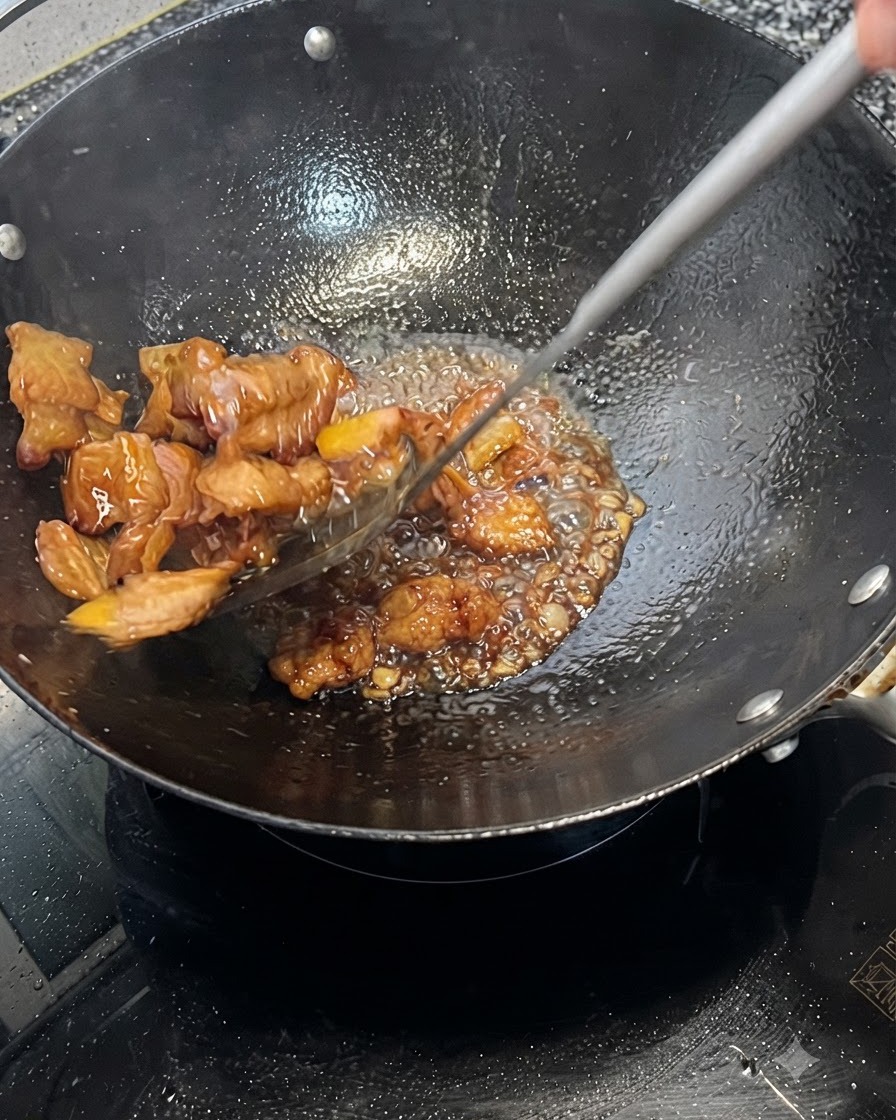 Pork belly being rapidly tossed and coated in a bubbling dark sauce in a wok.