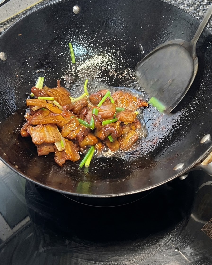 A spatula tossing pork belly and green onions together inside a hot wok.