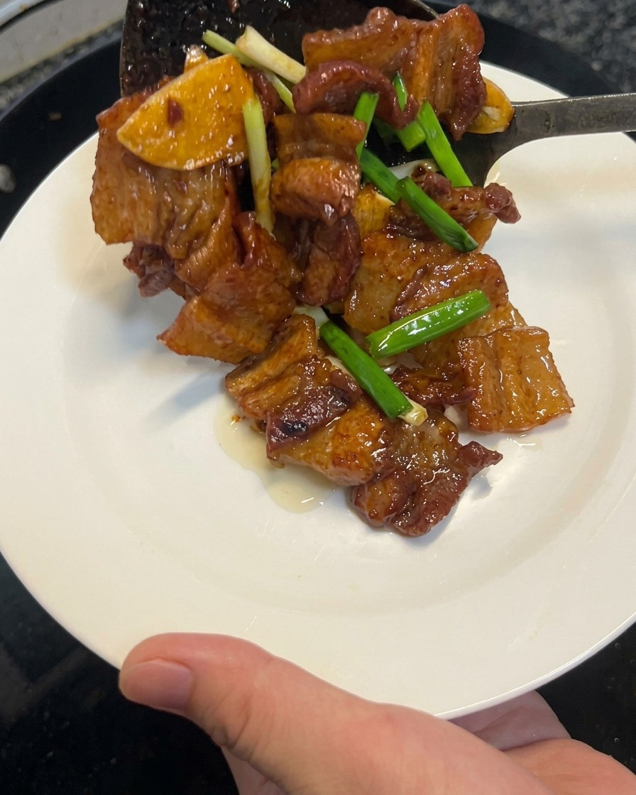 Cooked soy sauce pork belly being lifted out of a wok with a spatula onto a clean white plate.