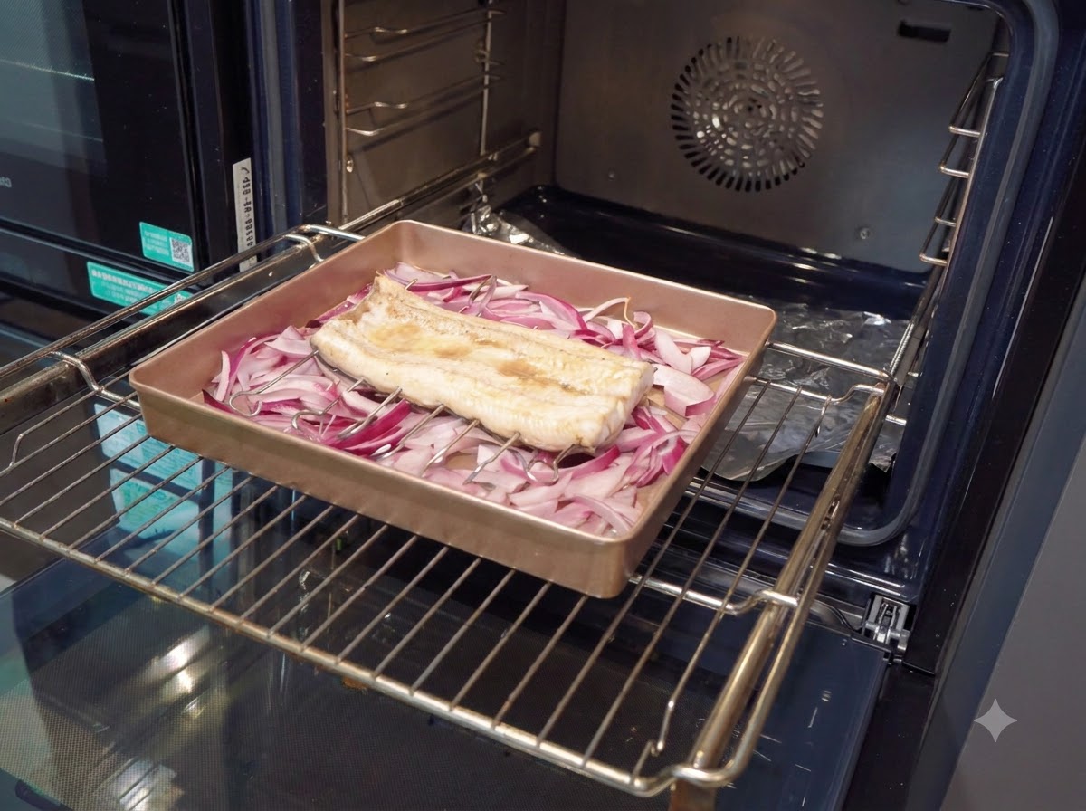 A pastry brush applying a thick, dark brown sauce onto a partially cooked eel fillet inside a baking pan.