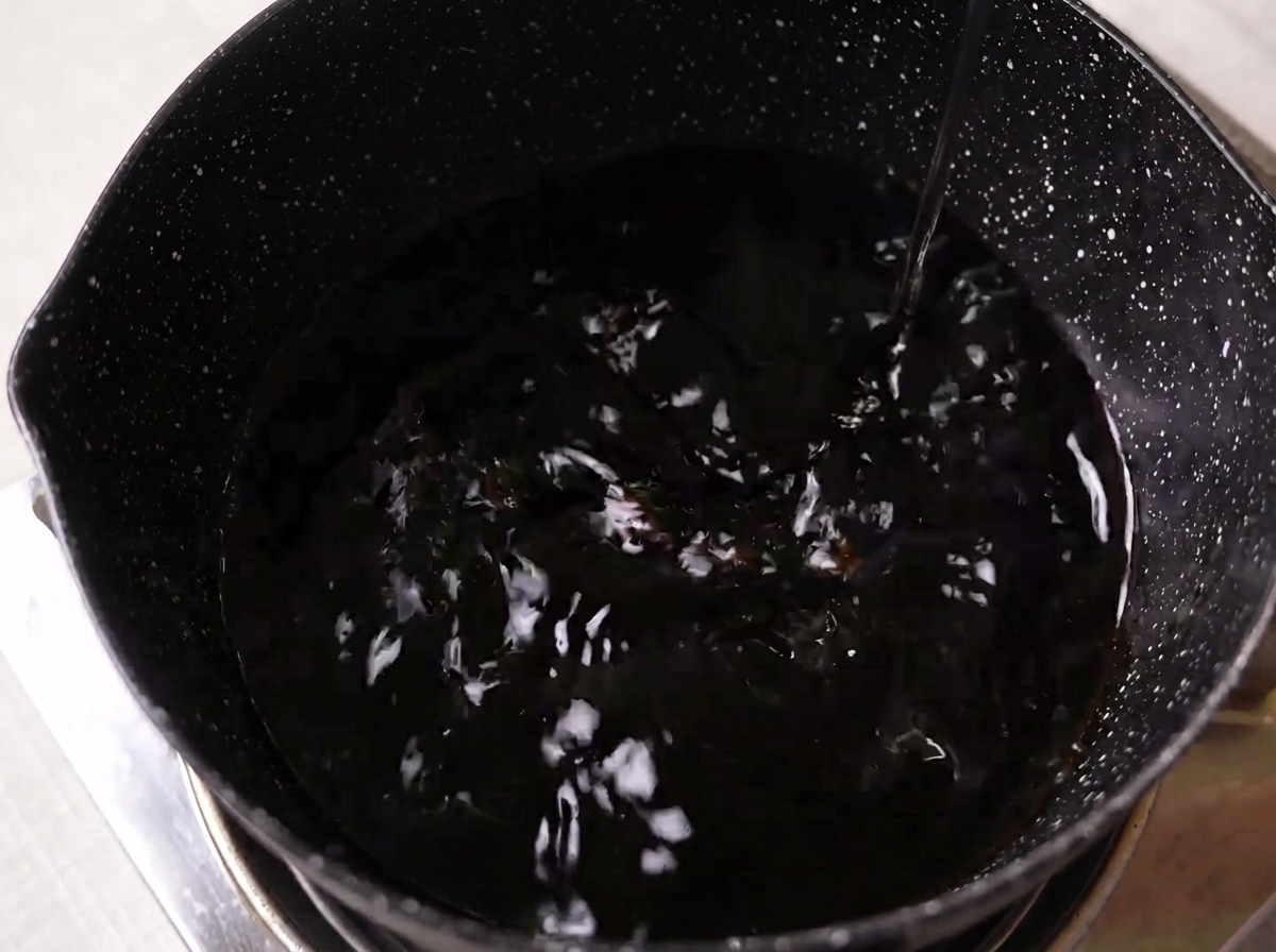 Soy sauce, mirin, sake, and white sugar mixing in a dark pot on a stovetop.