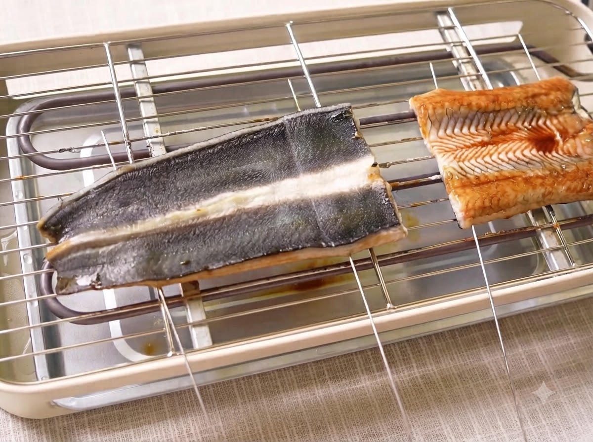 Eel fillets cooking on an electric grill with metal skewers piercing the meat.