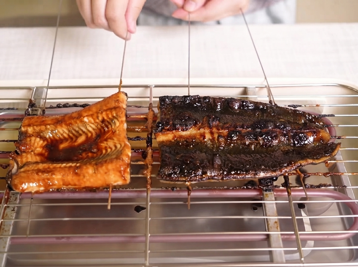 Browning eel fillets being brushed with a glossy dark sauce on a grill rack.