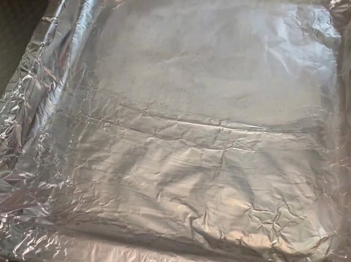 A metal baking pan lined with crumpled aluminum foil that has been brushed with a glistening layer of cooking oil.