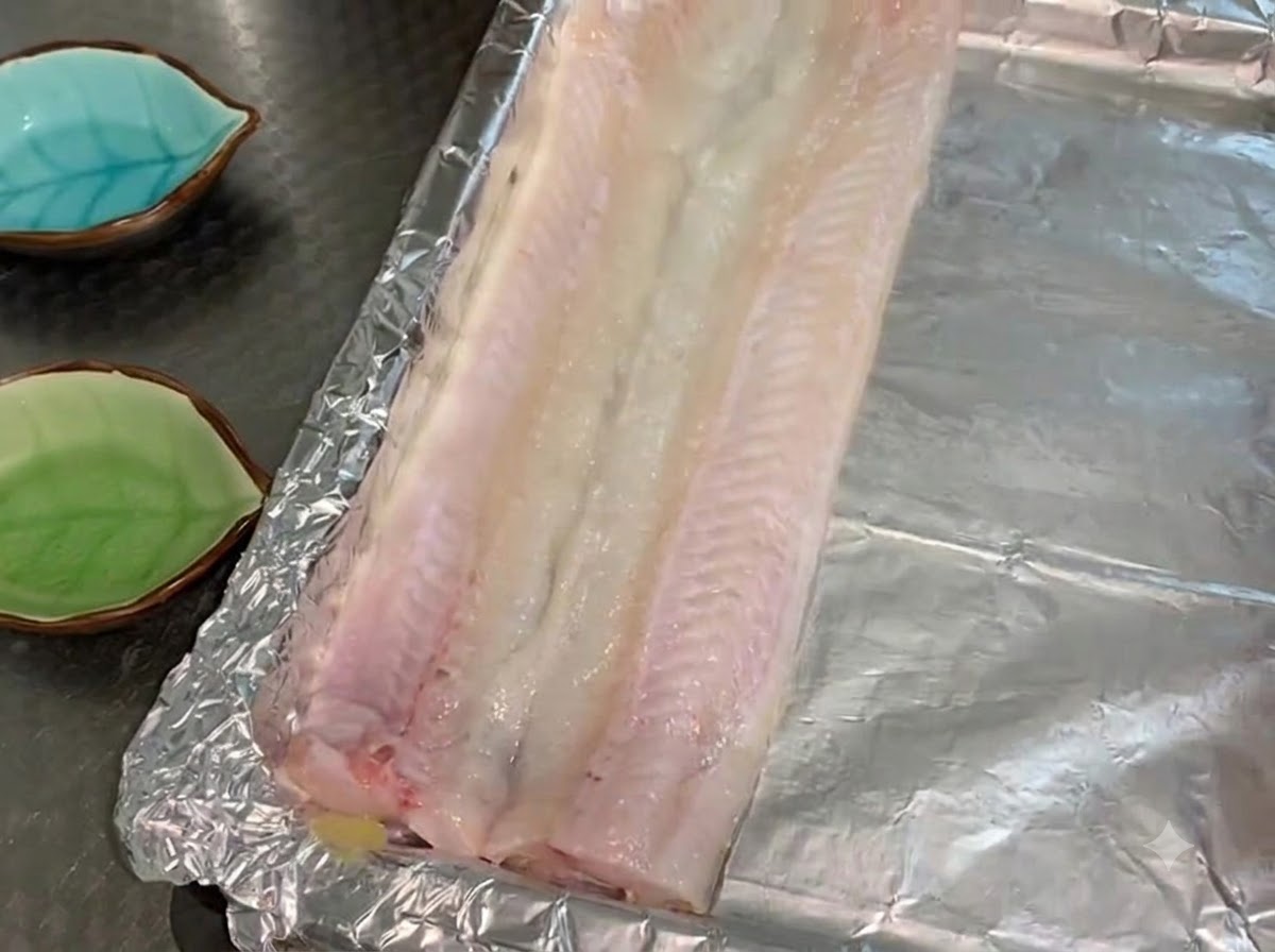 Raw eel fillets laid flat in a single layer on an oil-brushed foil-lined baking tray.