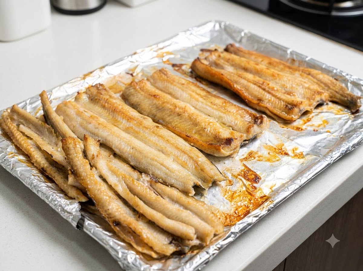 A close-up view of partially baked eel fillets being brushed with cooking oil on a baking tray.