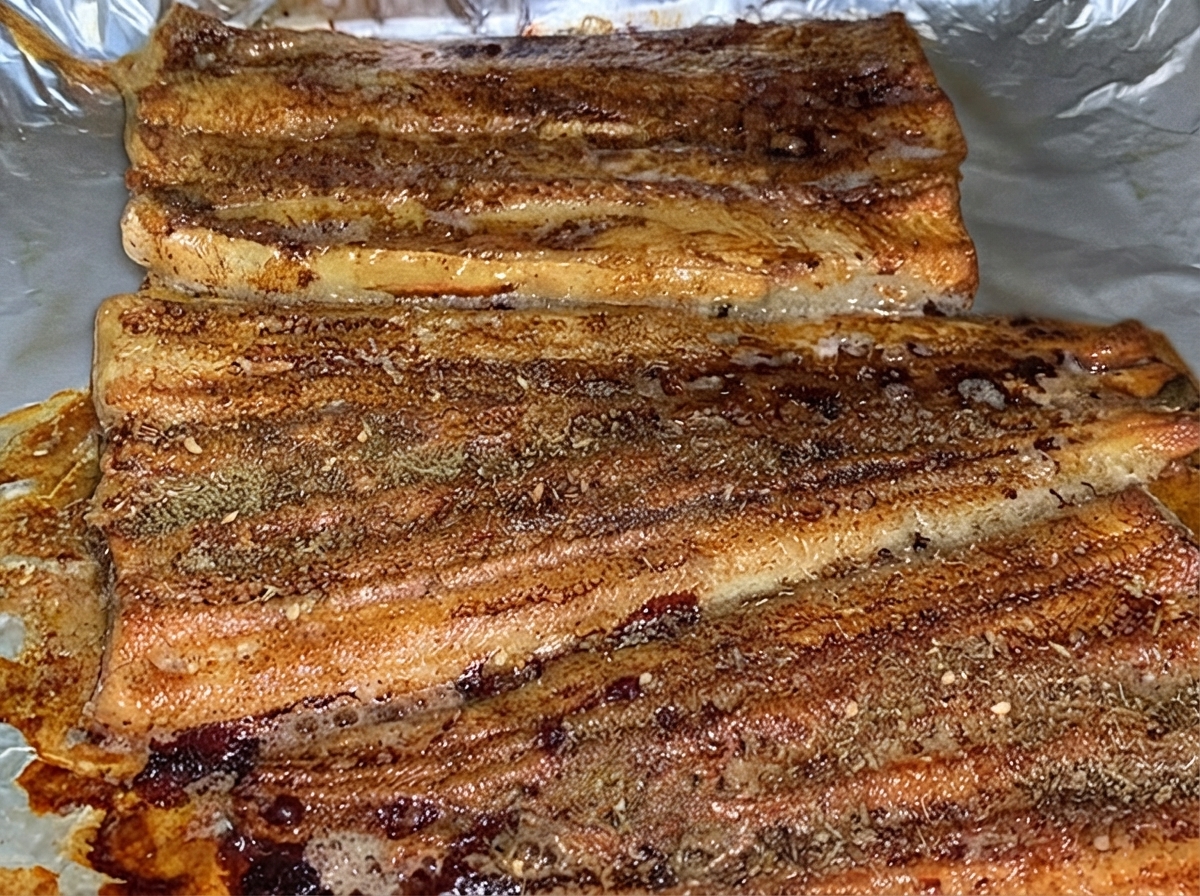 Baked eel fillets dusted evenly with a layer of brown BBQ seasoning powder inside a baking pan.