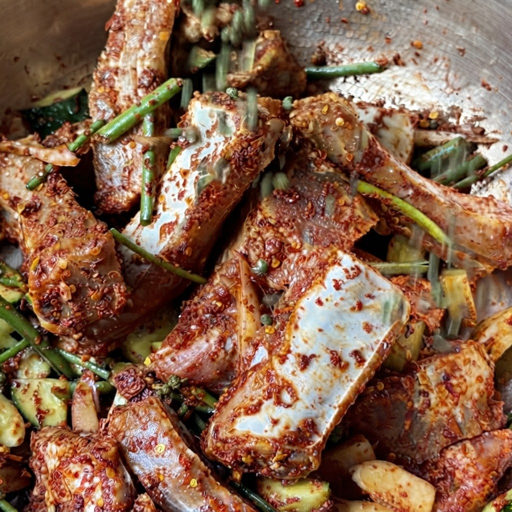 A handful of whole green Sichuan peppercorns falling onto the marinated pork ribs.