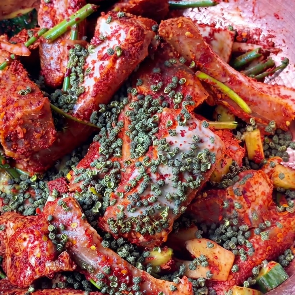 A close-up view of whole red Sichuan peppercorns scattered over the seasoned red meat pieces.