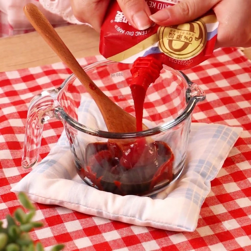 Chili paste being poured from a packet into a glass measuring cup containing other liquids.