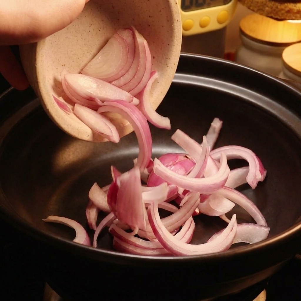 Red onion slices being poured from a ceramic bowl into a black pot.
