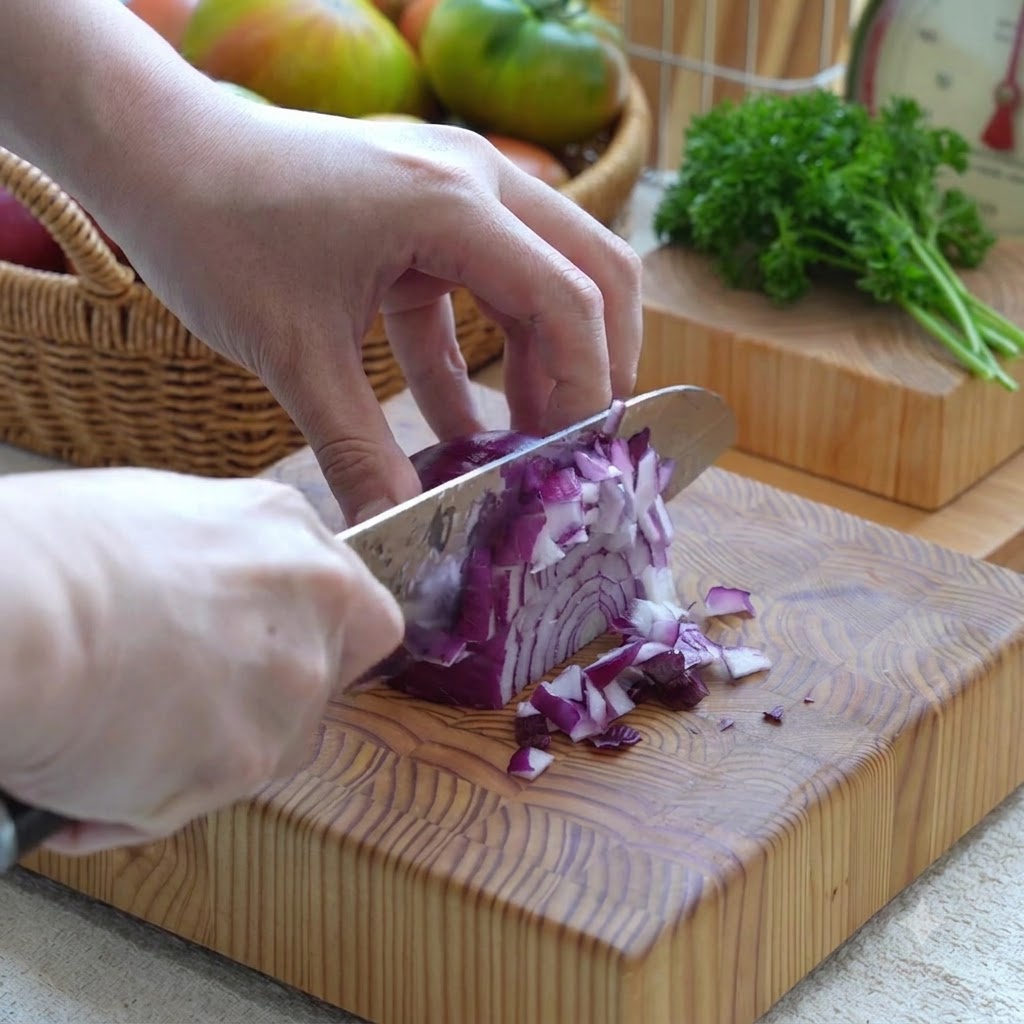 Red onion being diced into small pieces with a knife on a wooden board.
