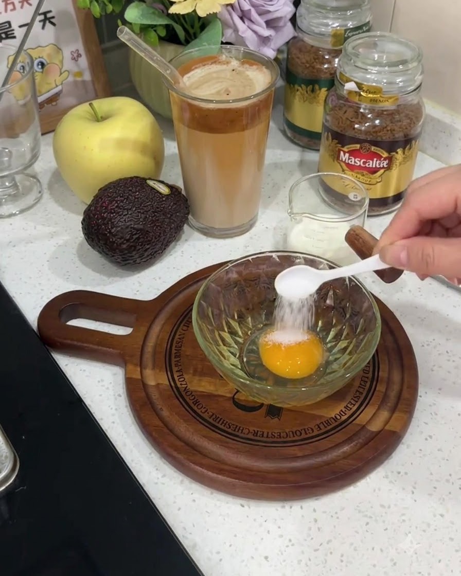 A small white spoon adding salt directly onto the yolk of a raw egg in a glass bowl.