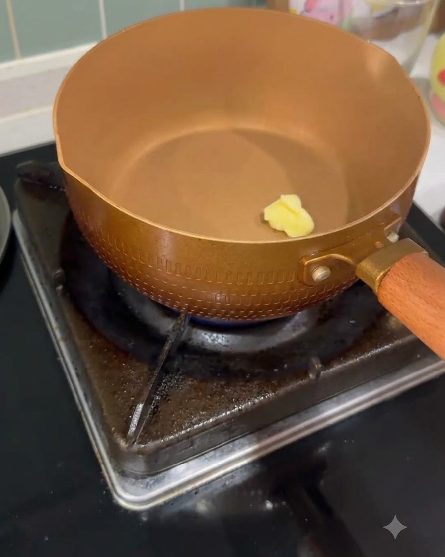 A small pat of butter melting inside a heated copper-colored saucepan on a gas burner.