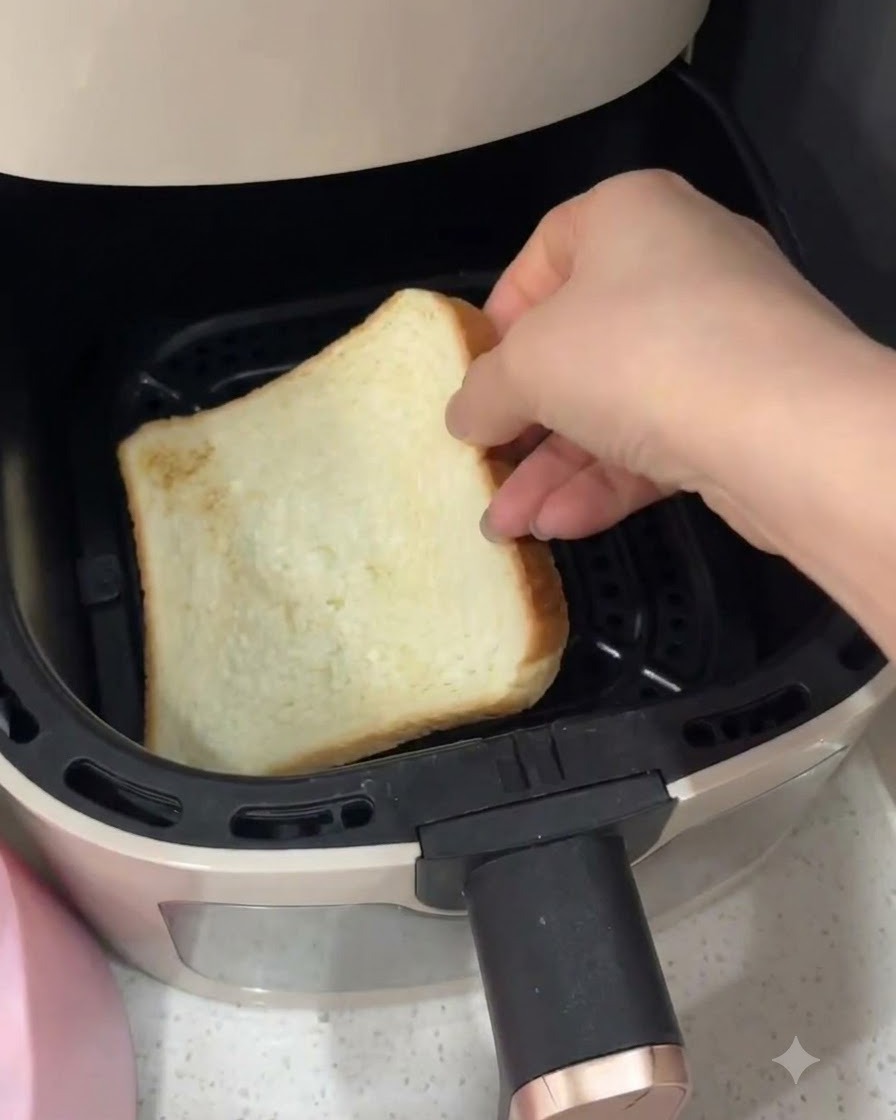 A hand placing a slice of white sandwich bread inside an air fryer basket.