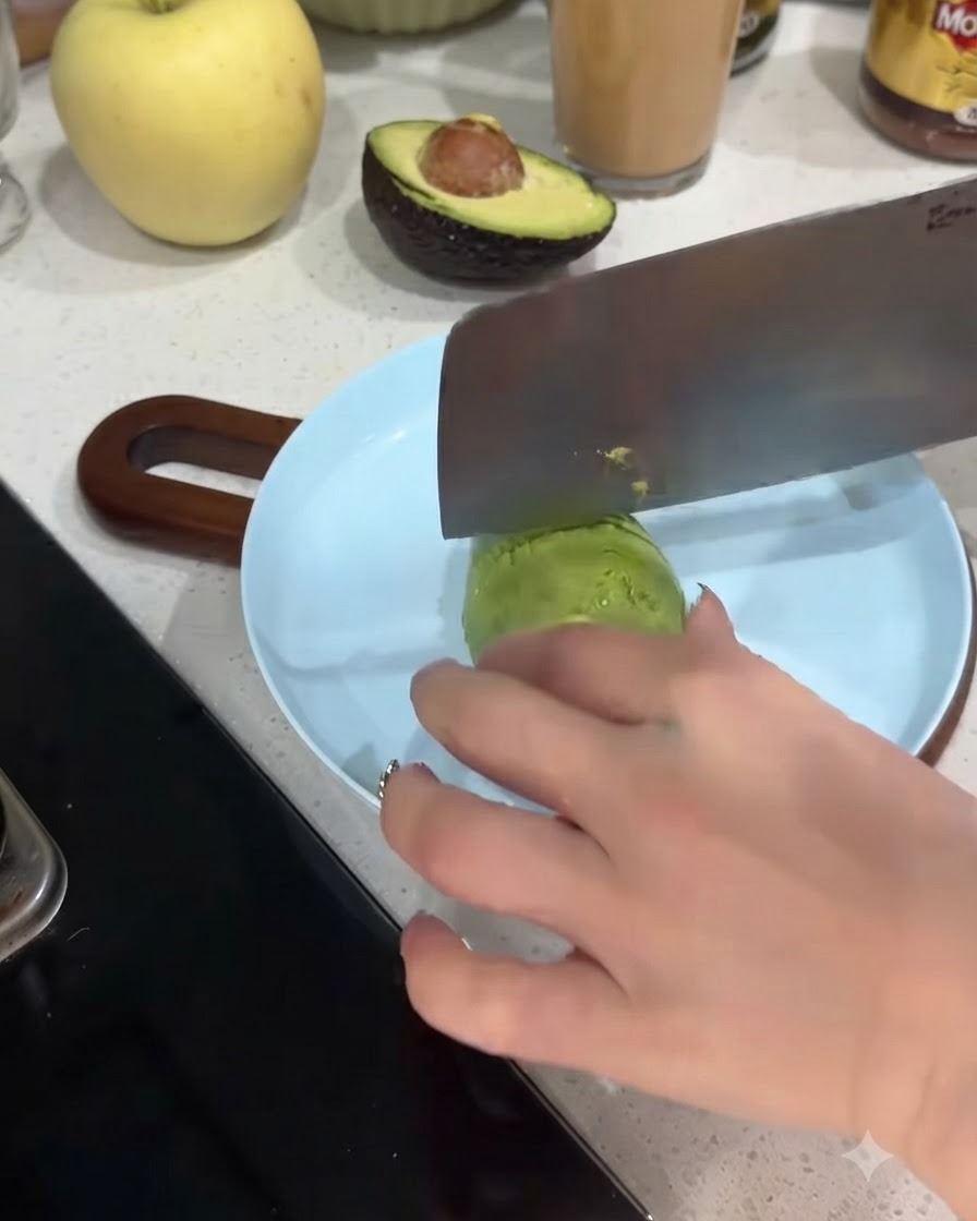 An avocado half being sliced into thin pieces on a light blue plate.
