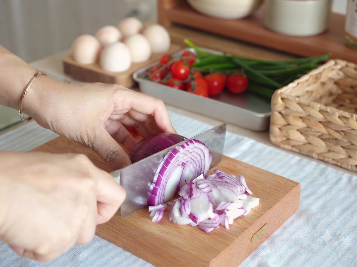 Green scallions being diced into small pieces with a knife on a wooden surface.